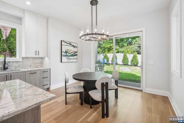 dining area with light wood-type flooring, an inviting chandelier, and sink