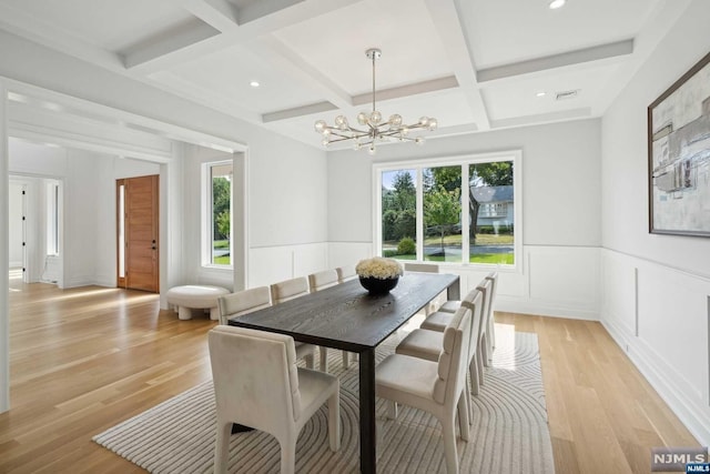 dining area with beamed ceiling, an inviting chandelier, light wood-type flooring, and coffered ceiling