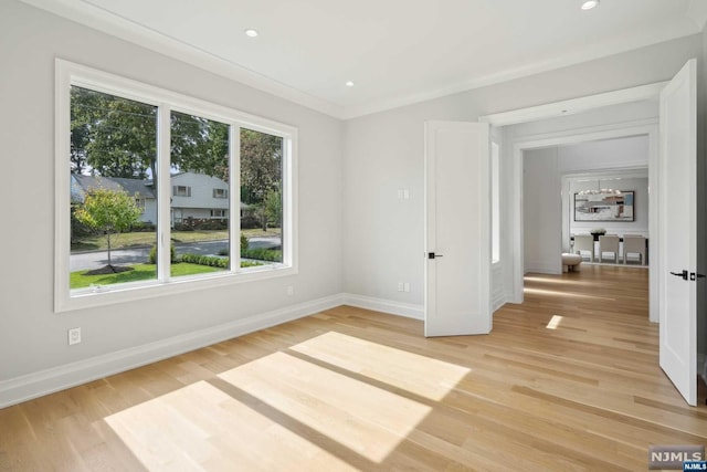 empty room featuring light wood-type flooring, crown molding, and a wealth of natural light