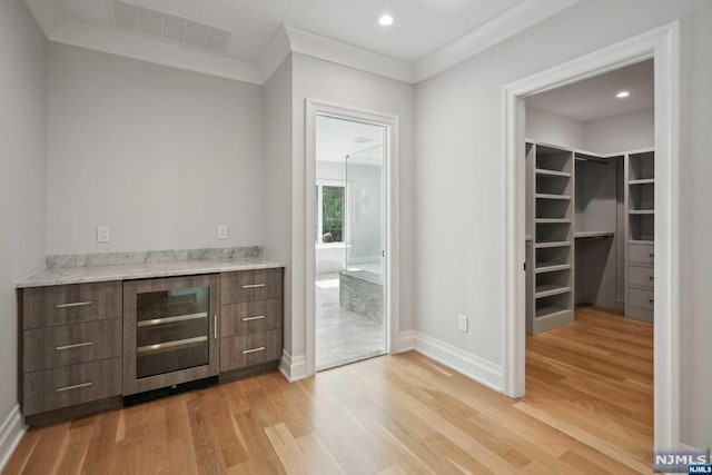 bar featuring dark brown cabinets, light hardwood / wood-style flooring, beverage cooler, and crown molding