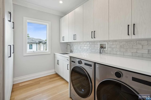 laundry area featuring washing machine and clothes dryer, light wood-type flooring, cabinets, and sink