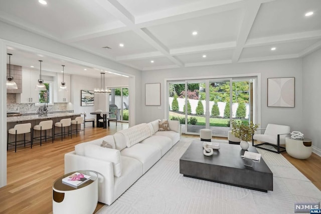 living room with a notable chandelier, light hardwood / wood-style floors, beam ceiling, and coffered ceiling