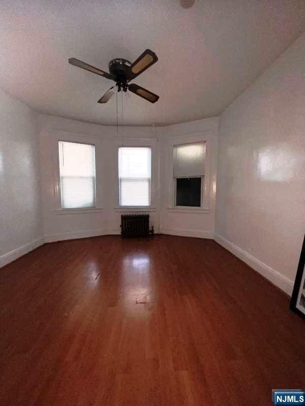 unfurnished living room with radiator heating unit, dark wood-type flooring, and ceiling fan