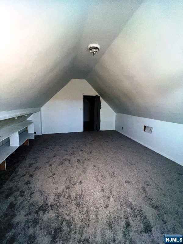 additional living space featuring vaulted ceiling and dark colored carpet