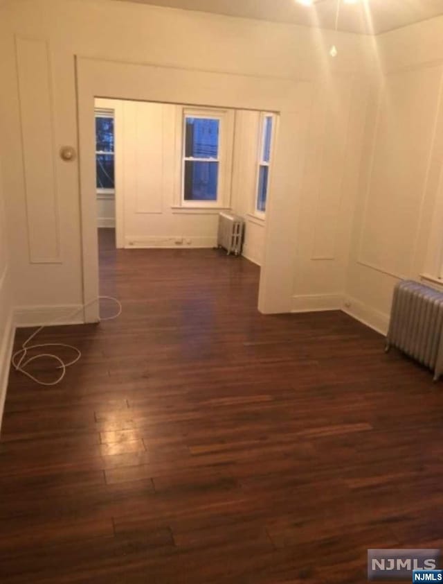 spare room with radiator heating unit and dark hardwood / wood-style floors