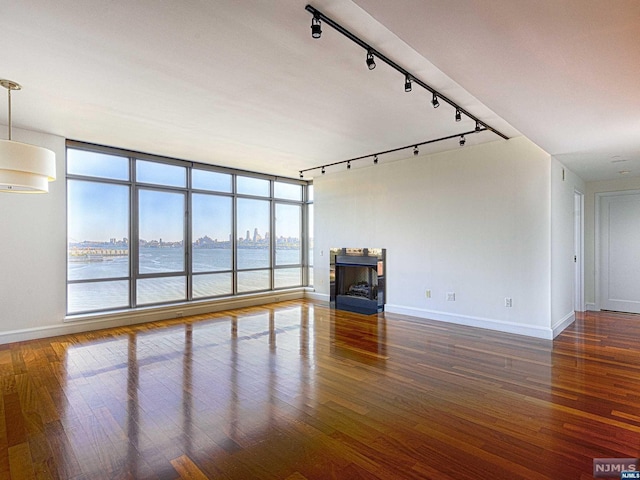 unfurnished living room with rail lighting, a water view, and dark hardwood / wood-style floors