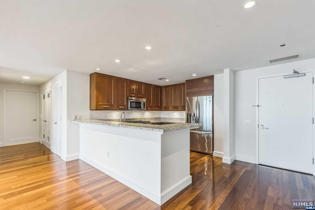 kitchen with kitchen peninsula, wood-type flooring, stainless steel appliances, and light stone countertops