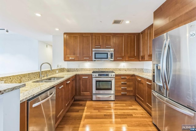 kitchen featuring sink, appliances with stainless steel finishes, light hardwood / wood-style floors, light stone counters, and kitchen peninsula