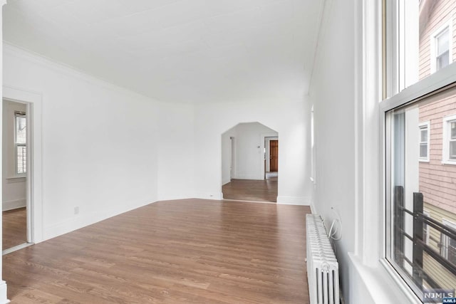 empty room with hardwood / wood-style floors, radiator heating unit, and ornamental molding