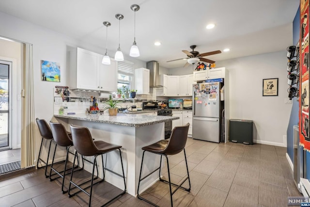 kitchen featuring a kitchen bar, appliances with stainless steel finishes, tasteful backsplash, wall chimney exhaust hood, and white cabinets