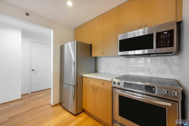 kitchen featuring decorative backsplash, appliances with stainless steel finishes, and light hardwood / wood-style floors