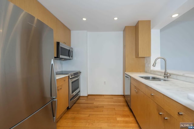 kitchen with sink, light stone countertops, stainless steel appliances, and light hardwood / wood-style flooring