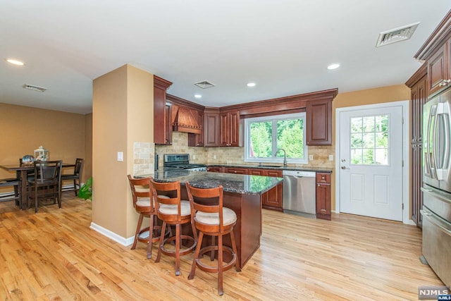 kitchen with light hardwood / wood-style flooring, backsplash, premium range hood, a kitchen bar, and appliances with stainless steel finishes