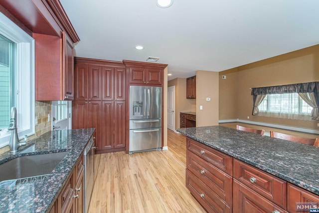 kitchen with backsplash, dark stone counters, stainless steel appliances, sink, and light hardwood / wood-style floors