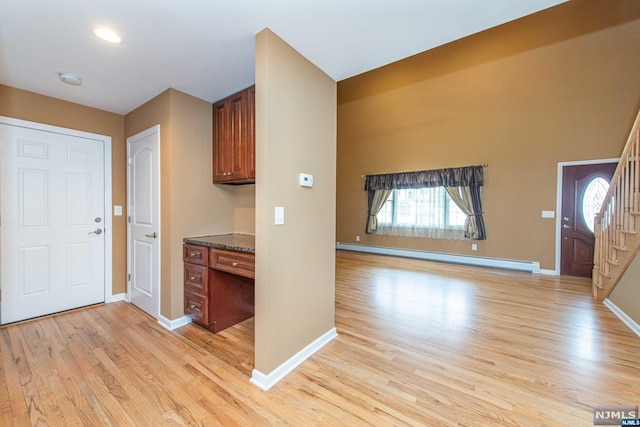 foyer entrance featuring baseboard heating, built in desk, and light wood-type flooring