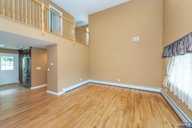 empty room with light hardwood / wood-style flooring, a high ceiling, and a baseboard heating unit