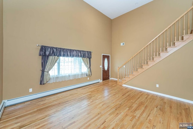 foyer entrance with light wood-type flooring, a towering ceiling, and a baseboard heating unit