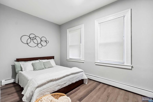 bedroom featuring hardwood / wood-style floors and a baseboard heating unit