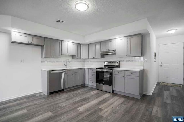 kitchen with gray cabinetry, dark hardwood / wood-style floors, backsplash, a textured ceiling, and appliances with stainless steel finishes