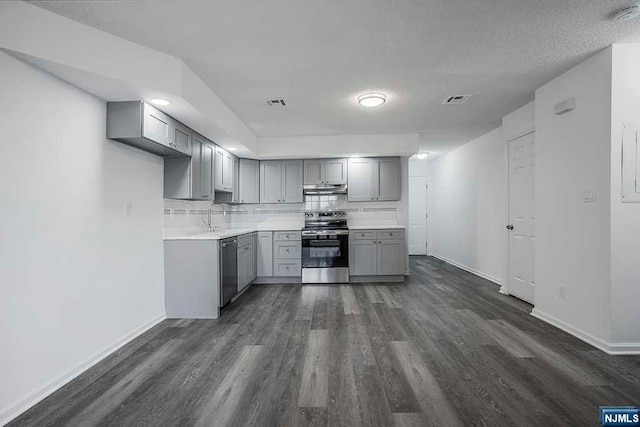 kitchen with tasteful backsplash, a textured ceiling, stainless steel appliances, gray cabinets, and dark hardwood / wood-style floors