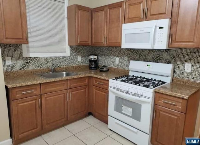 kitchen with decorative backsplash, white appliances, sink, light tile patterned floors, and stone countertops