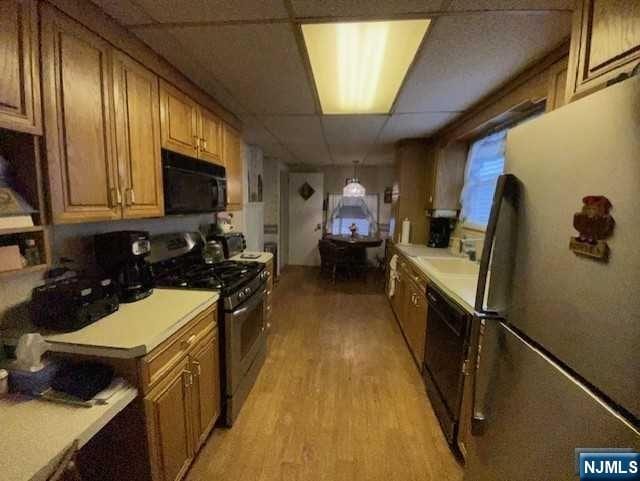 kitchen with a paneled ceiling, black appliances, and light hardwood / wood-style floors