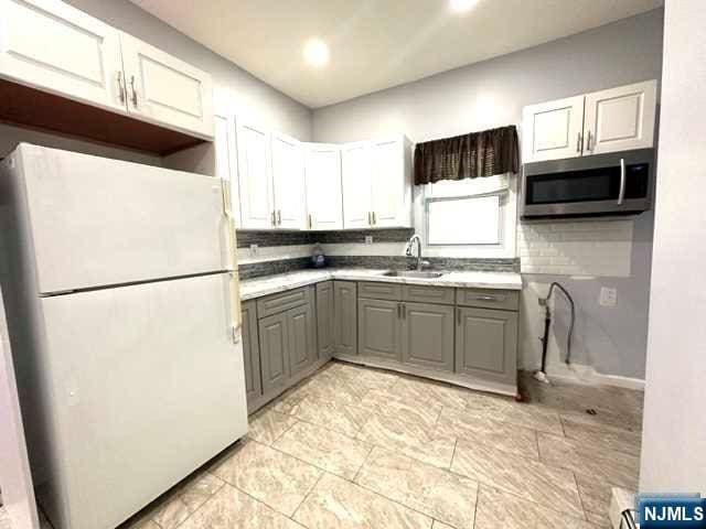 kitchen featuring gray cabinetry, backsplash, sink, white fridge, and white cabinetry