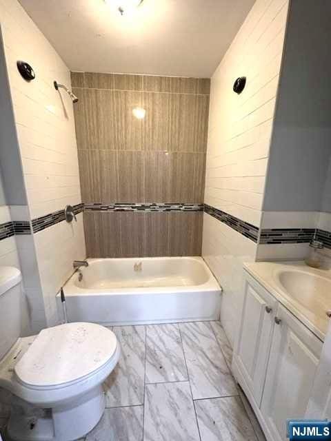 full bathroom with tiled shower / bath combo, toilet, tile walls, and vanity