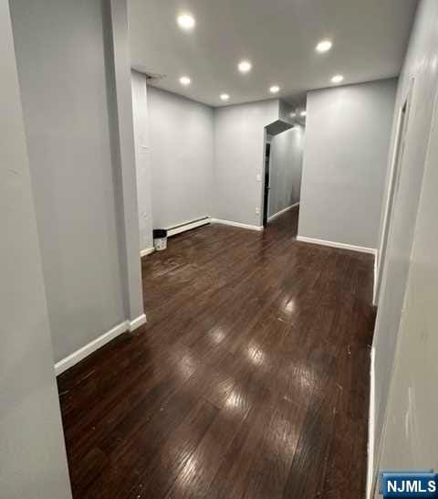 empty room with baseboard heating and dark wood-type flooring