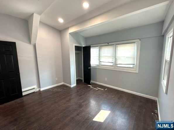 unfurnished bedroom with dark hardwood / wood-style flooring and baseboard heating