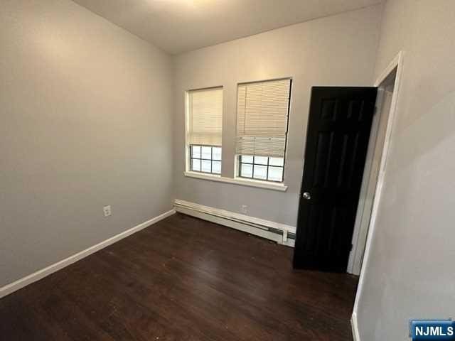 unfurnished room featuring a baseboard radiator and dark hardwood / wood-style floors