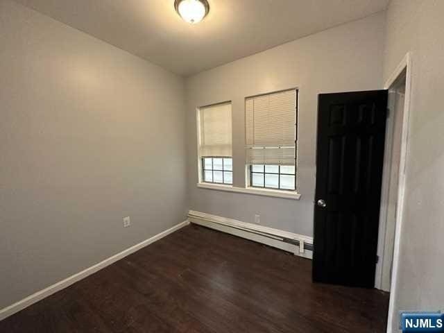 spare room featuring dark hardwood / wood-style flooring and a baseboard heating unit