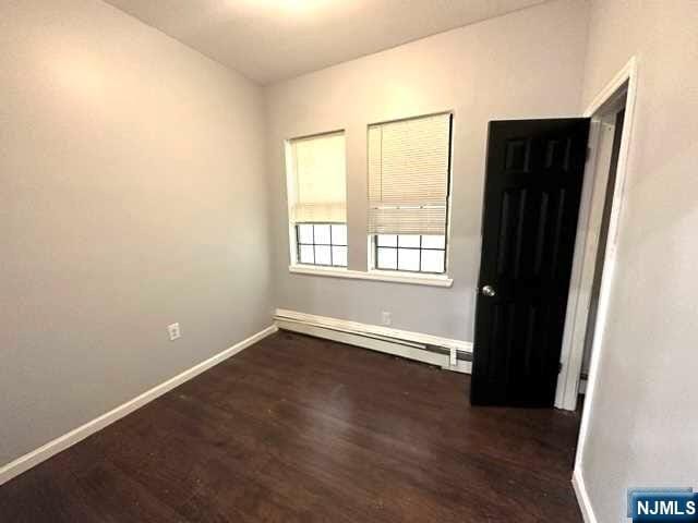 empty room featuring baseboard heating and dark wood-type flooring