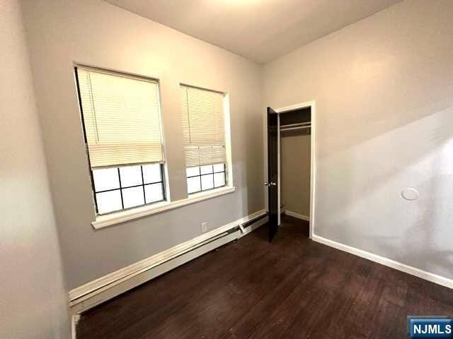 unfurnished bedroom with a closet, dark hardwood / wood-style flooring, and a baseboard radiator