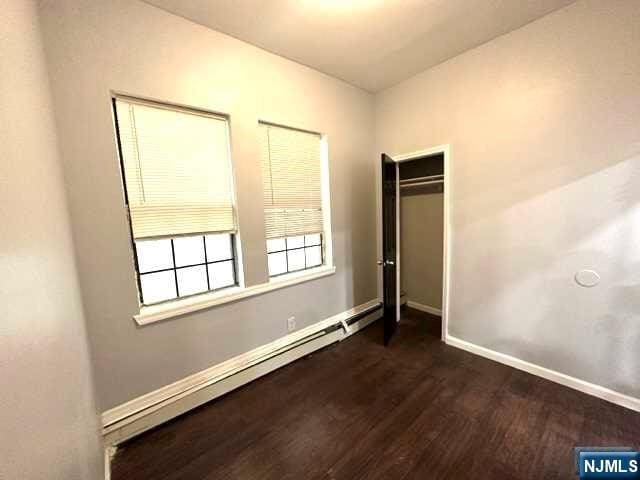 unfurnished bedroom with a closet, dark hardwood / wood-style flooring, and a baseboard heating unit