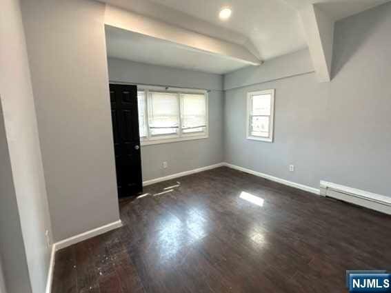 unfurnished room with dark wood-type flooring and a baseboard radiator