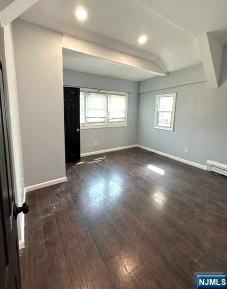 spare room featuring beam ceiling and dark wood-type flooring