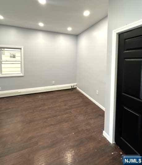 unfurnished room featuring dark wood-type flooring and a baseboard radiator