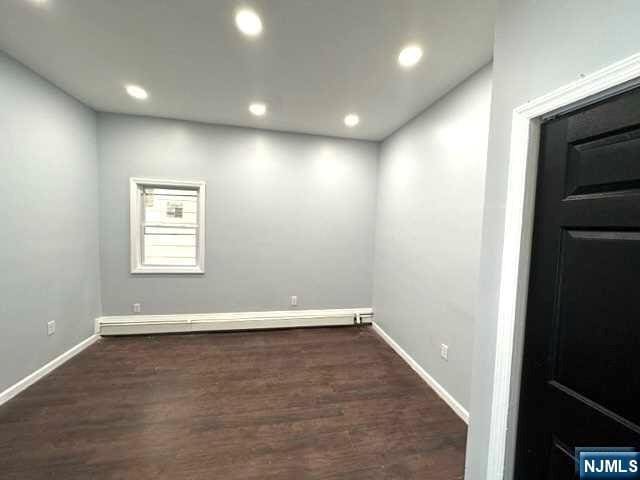 unfurnished room featuring baseboard heating and dark hardwood / wood-style floors