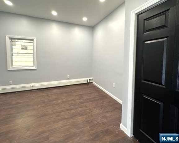 unfurnished room with a baseboard radiator and dark hardwood / wood-style floors