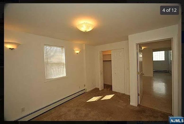 unfurnished bedroom featuring dark carpet, a closet, and a baseboard heating unit