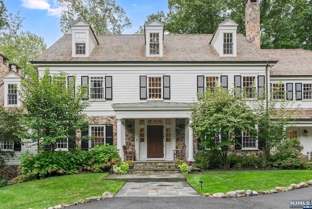 view of front of property featuring stone siding, a chimney, and a front lawn