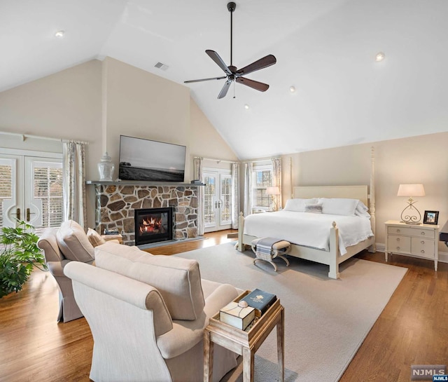 bedroom featuring access to exterior, ceiling fan, a stone fireplace, high vaulted ceiling, and light wood-type flooring