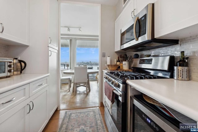 kitchen featuring appliances with stainless steel finishes, backsplash, track lighting, light hardwood / wood-style flooring, and white cabinetry