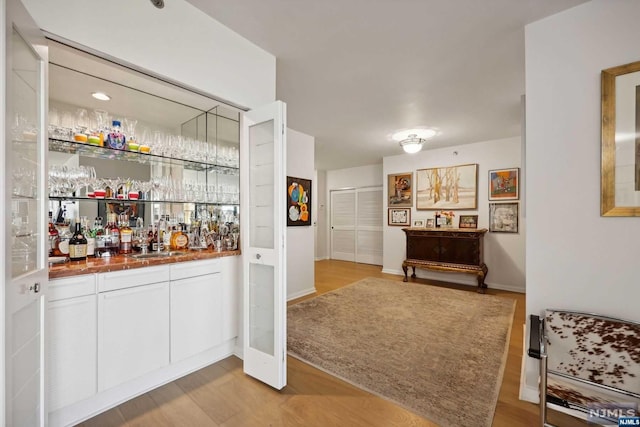 bar with white cabinets, light hardwood / wood-style floors, and sink