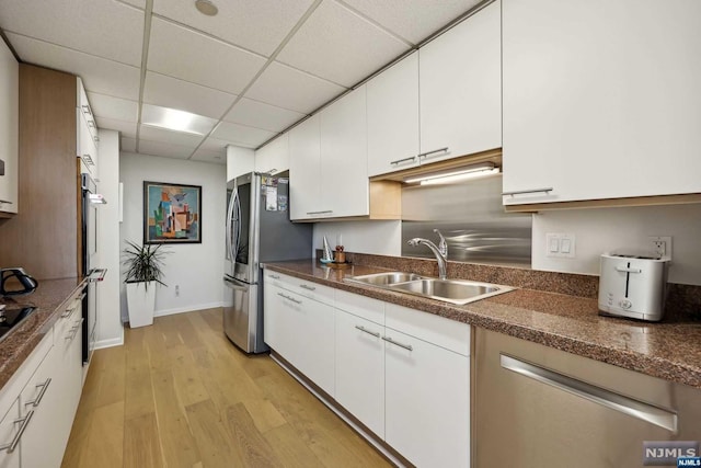 kitchen with stainless steel refrigerator, a drop ceiling, sink, light hardwood / wood-style flooring, and white cabinets