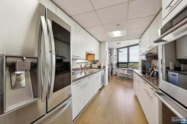 kitchen with stainless steel appliances, white cabinetry, a drop ceiling, and light hardwood / wood-style floors