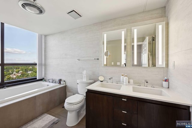 bathroom featuring tile patterned flooring, toilet, a bathtub, vanity, and tile walls