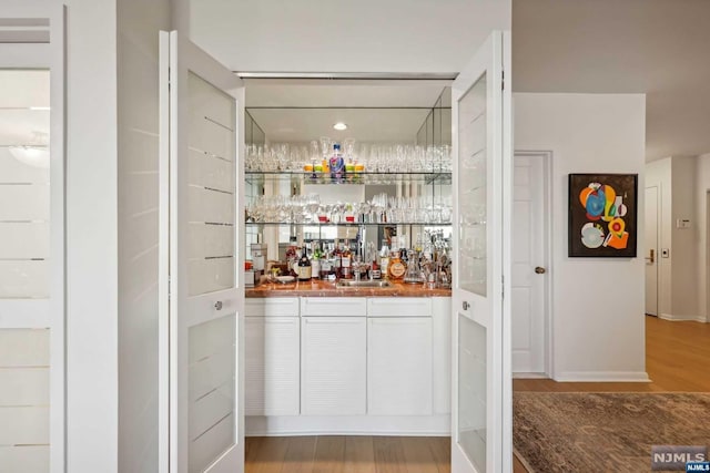 bar with white cabinets, hardwood / wood-style floors, and sink