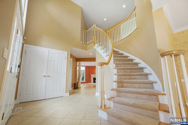 staircase featuring tile patterned flooring, ornamental molding, and a high ceiling